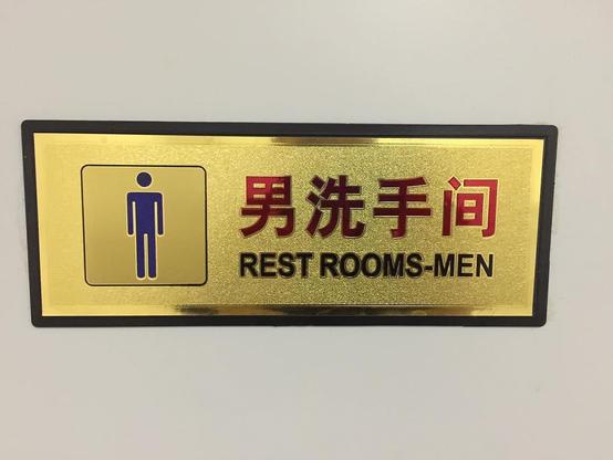 This picture shows a signboard indicating a men's restroom. The sign is written in both Chinese and English languages. The sign has an icon of a man, and there is an arrow pointing to the right side of the image.