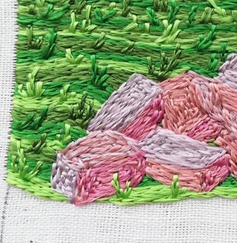 Close up of the grass, three shades of green, working around the pile of building stone in pinky orangey shades.