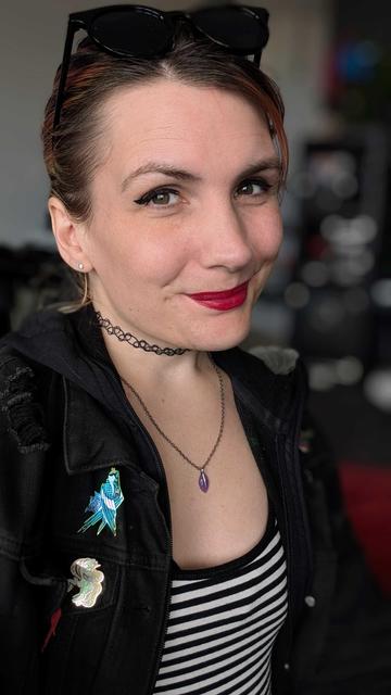 Ash, a trans woman, smiles warmly at the camera.