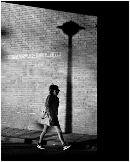 A person walking. There’s a shadow of a street lamp. Photo in black and white.