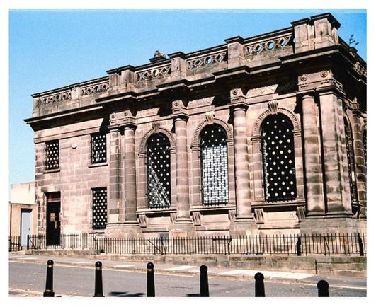 Colour photograph showing a former Victorian bank building, big arch windows and columns, beneath a blue sky.