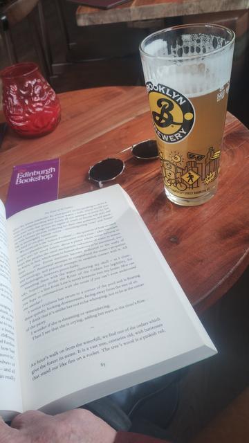 Book lying open on a table next to a pint of ale