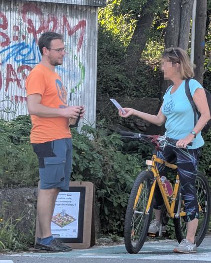 Photo: un homme blanc à pied, en train de parler à une dame à vélo, qui vient de recevoir un tract et est en train de le lire.