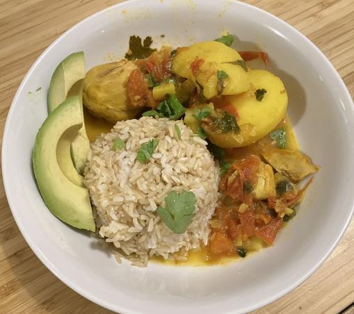 A bright yellow chicken and potato stew served with rice, avocado, and cilantro.