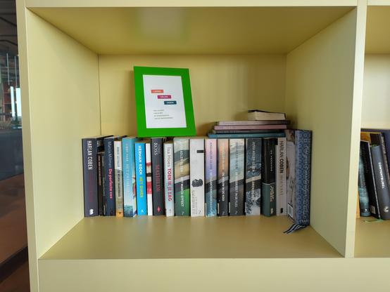 Boekenplank met boeken met daarop een bordje Lenen, Delen, Doen!