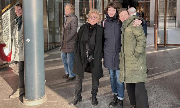 Beate Müller-Gemmeke steht mit zwei Kolleginnen vor einem modernen Gebäudeeingang. Alle drei sind warm angezogen und lächeln in die Kamera. Im Hintergrund sind weitere Personen aus der Arbeitsgruppe zu sehen. Die Atmosphäre wirkt herzlich und vertraut.