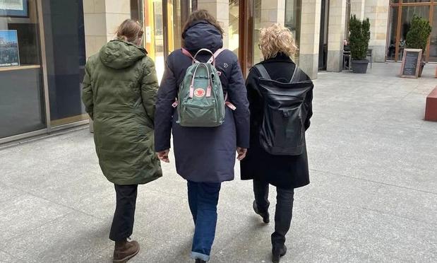 Beate Müller-Gemmeke läuft gemeinsam mit zwei Kolleginnen durch eine moderne, urbane Umgebung. Sie sind von hinten zu sehen, tragen Rucksäcke und warme Jacken. Das Bild vermittelt Gemeinschaft und Zusammenhalt.