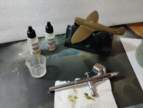 Spitfire MKI recien barnizado en mate para proteger la pintura. Se ven el aerografo, un bote de barniz Vallejo, un bote de disolvente Vallejo y un vasito con un poco de agua.
