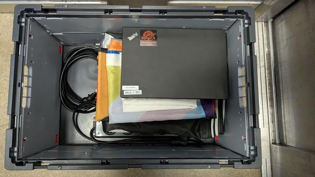 Eine Halbvolle Eurobox von oben mit Laptops, Kabeln, und zusammen-gelegten Flaggen