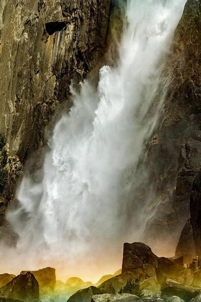 Waterfall Glow

This is an image of the Lower Yosemite Falls base. Located of course in Yosemite Valley. 
This is a closeup image of the falls, only focusing on the last 50-75 feet.
The fall is framed on both sides with  dark gray/brown granite cliffs.
The water kicks out just a bit as it hits the bottom and that is where the focus of the image is.
You can see the affects of water hitting off the rocks and shooting up and to the side creating almost waves of water coming down.
At the bottom of the falls there is the beginning of a rainbow that is forming as the morning sun is rising in the sky.