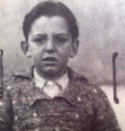 A photo of a young boy wearing a jacket and a shirt buttoned at the top. He has short hair and slightly opened mouth.