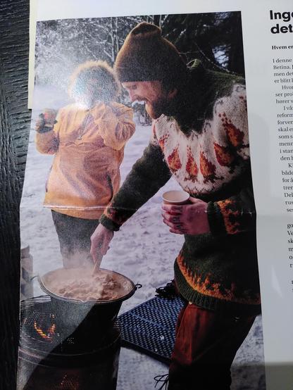 From a magazine: a man makes food on a campfire, wearing a sweater with a campfire pattern