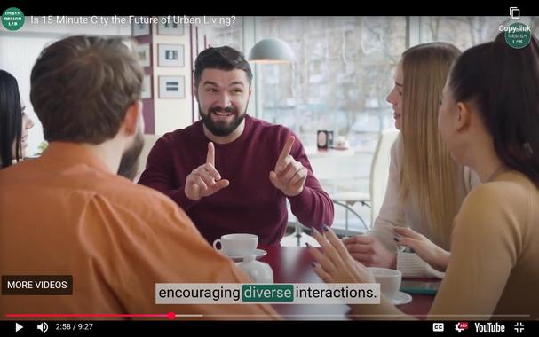 Screenshot from a youtube video from the "Urban Design Lab." The video is titled "Is 15 Minute City the Future of Urban Living?" 
The image shows a college-aged white male, facing the camera, smiling and gesturing at 4 similarly-aged white people, in what appears to be a coffee shop.