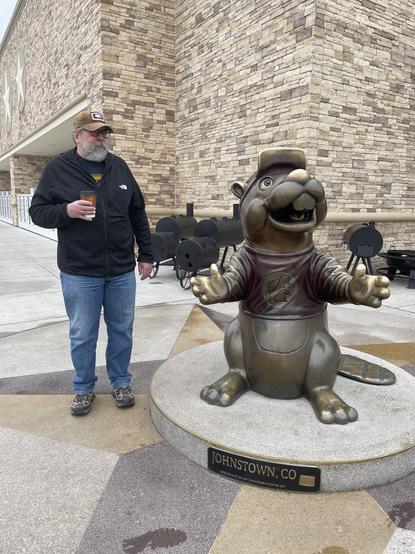 Milcom Miasma himself standing in fear and grave concern next to a bronze statue of Buc-ee a cartoon beaver that is the mascot for Buc-ee's convenience stores and gas stations. Behind me and the statue is a truly massive Buc-ee's store in Johnstown, Colorado.