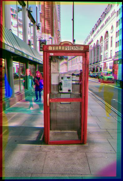 A color trichrome photo of a red vintag telephone booth surrounded by c,m,y ghost people and cars.