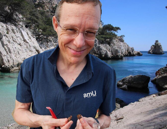 Avi Loeb dans les calanques avec un T-shirt AMU montre les fragments de météorite alien qu'il va immerger au milieu de nos poissons.