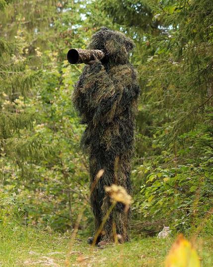 Wildlife photographer in a ghillie suit standing and holding a camera