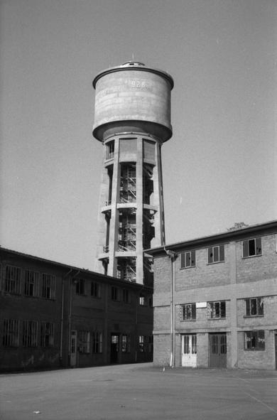 Black and white photography in portait of a water tower. The picture has been shot from an abandoned factory yard.