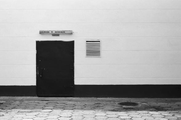 Drzwi na tle białej ściany, nad drzwiami napis "Człowiek w komorze"