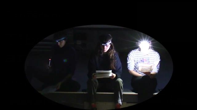 Capture d’écran : trois intervenant⋅es lisent un texte dans le noir, éclairé⋅es par une lampe frontale.