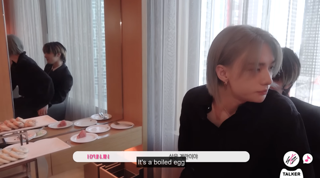 In a hotel room, Hyunjin sits on I.N's lap. They're visible in the mirror to one side as well. Caption: "It's a boiled egg"