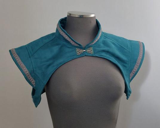 Boléro medfan couleur bleu/vert canard avec des galons et un fermoir argenté. Vue de devant.