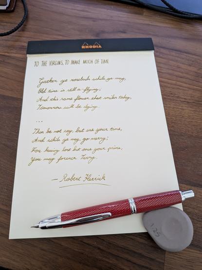 A picture of a Pilot Capless fountain pen in textured red with silver trim.  The nib is protruding to the left of frame, with the pen held in place by an eraser.

The pen is on an open Rhodia pad with black at the top of the pad and 'Rhodia' in orange.  The paper is off-white beige.  Golden Ina-Ho ink on the page depicts the first and last verses of To the Virgins, to Make Much of Time by Robert Herrick.  The title is in tall and thin caps, with the verses in roundhand copperplate script.  I've signed the bottom 'Robert Herrick' and underlined it.