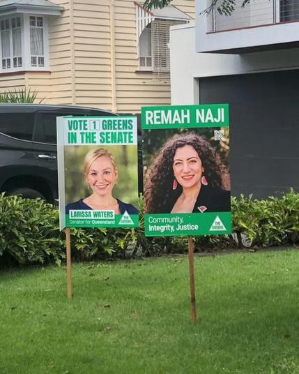 Yard signs for Larissa Waters and Remah Naji on a front lawn. Larissa's sign says "Vote [1] Greens in the Senate" with a picture of Larissa and her name on it. Remah's sign says "Remah Naji", with a picture of Remah and "Community, Itegrity, Justice" below.