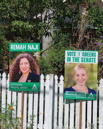Yard signs for Remah Naji and Larissa Waters on a white fence. Larissa's sign says "Vote [1] Greens in the Senate" with a picture of Larissa and her name on it. Remah's sign says "Remah Naji", with a picture of Remah and "Community, Itegrity, Justice" below.