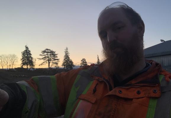 A cis white male who is broad and has a red beard offers a hug. He wears a reflective jacket
