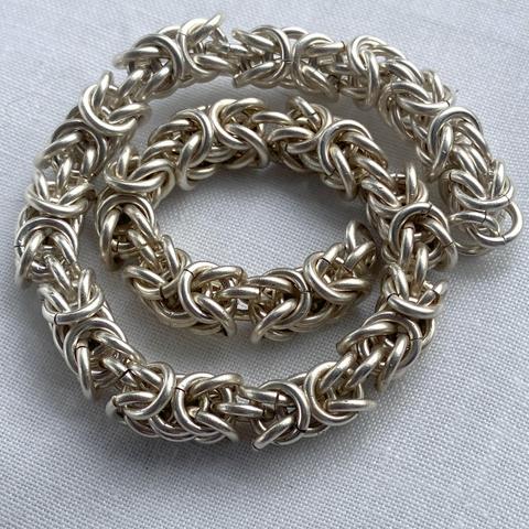 A silver chainmail bracelet with no fastener, coiled on a white cloth.
