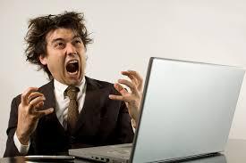 Image shows a man dressed in a suit and tie screaming in exasperation at an open laptop.