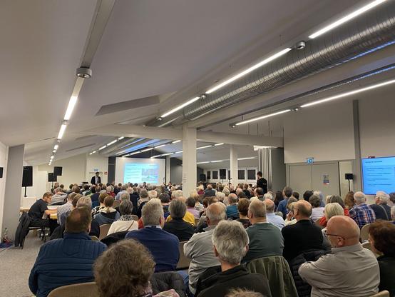 Blick von hinten in den Richard-Clauß-Saal im Bürgerhaus RSKN. Über voll besetzte Stuhlreihen hinweg ist OB Matthias Klopfer am Rednerpult zu sehen, dem Publikum zugewandt. Schräg hinter ihm eine Leinwand, auf der eine Folie zu sehen ist.