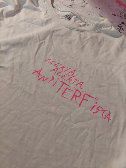 The top of a white shirt, with 'Alerta, Alerta, AntiTERFista printed in pink on it.