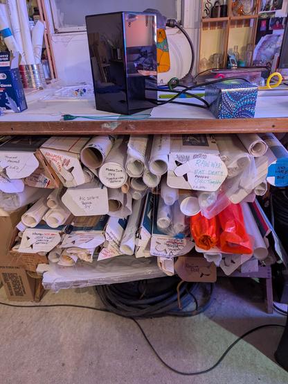 A bunch of Bruce Nauman patterns on non-asbestos paper. The patterns for some of my all time favorite pieces of neon- all rolled up under that table