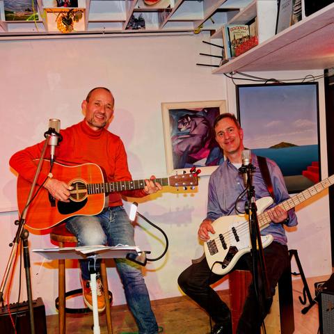 Ein Gitarrenspieler und ein E-Bass-Spieler auf einer kleinen Bühne