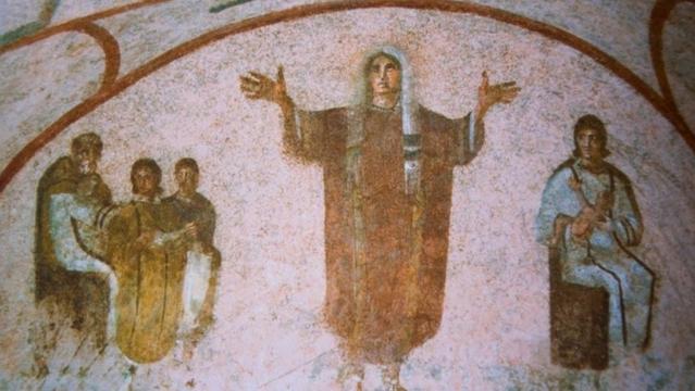 A fresco in the Catacombs of Priscilla, Rome, shows the figure of a woman raising her hands in prayer, surrounded by seated figures to the right and left