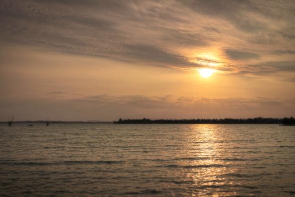 Photograph of the sun setting over a natural water reservoir.