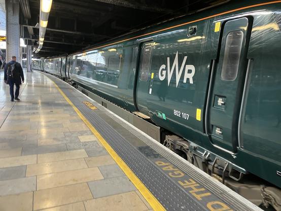 A railway station platform. To the right is a dark green train, with “GWR” in tall silver letters.