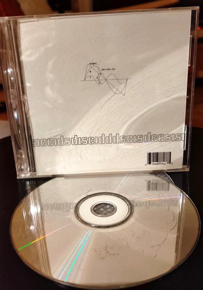 White CD cover. Minimalist design. Some sinus curves on a line in the middle with some letters and matematic formulas. 

"disc" written on the lower part. and the letters d i s c in different mixed order in front and behind of it, in gray. 

barcode in lower right corner, with the name of the release in small (GaijinCD4).

A cracked CD facing up, laying in front.