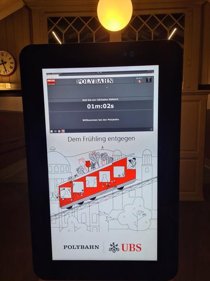 Abfahrtsanzeiger der Polybahn mit Frühlingsgruss und Sponsorlogo der schweizer Grossbank