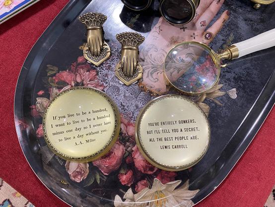 The quote is written on a surface under a glass sphere, which magnifies the image. 

A magnifying glass and other items appear on a tray alongside the object.