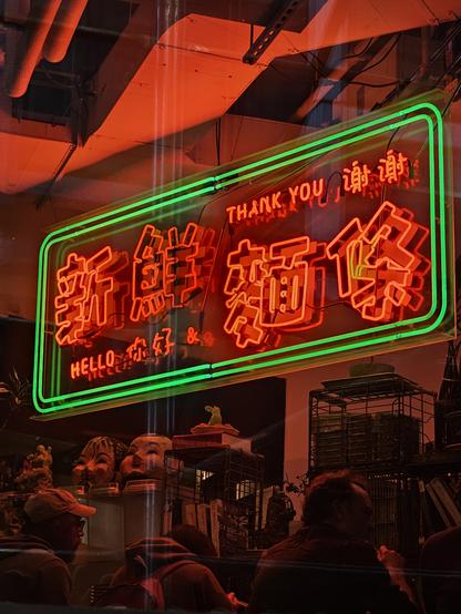 Sign in Neon hanzi (which i cant read) with letter forms that hace a stable sroke width (San Serif?) Outlined in red deon and some english text for 'heklo' and 'thankyou'