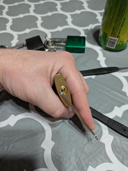 A tension wrench in the open position after a padlock was just picked. Other open locks and lock picks are in the background.