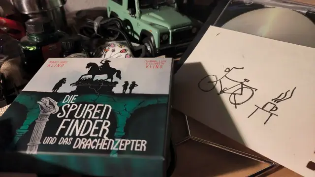 CD-Box des Hörbuches: Die Spurenfinder und das Drachenzepter. Daneben eine Kritzelzeichnung mit Fahrrad und einem Tisch mit Kaffeepott.