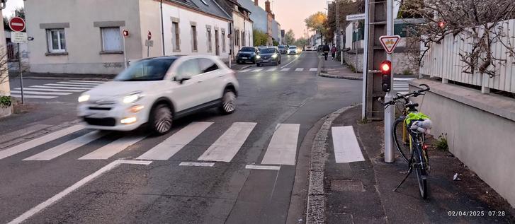 Une bicyclette est arrêtée à un feu dans un faubourg d'Orléans. À sa droite, il y a la gendarmerie, à sa gauche, les sévices techniques de la métropole.