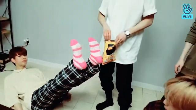 Seungmin lays on the floor and sticks hs legs in the air to show off his pink and white striped socks