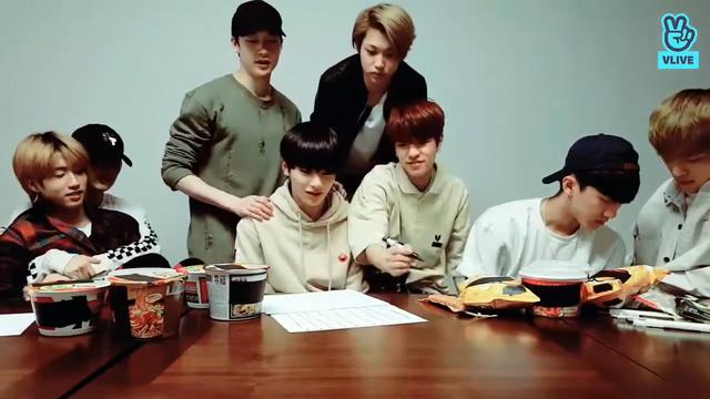 skz members behind a low table, with Seungmin about to draw on some paper. Lee Know has a peaceful and settled Han on his lap, with arms around him holding him firmly.