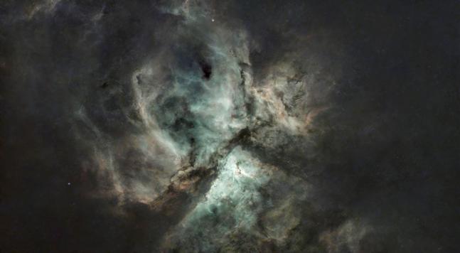 A starless nebula, roughly divided in three by an inverted 'Y' of dust lanes. The centre is a blue green, fading to a pinky-orange around the edges.
