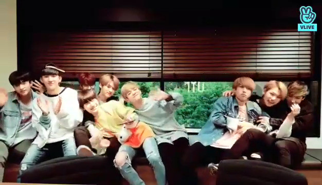 skz members sitting on a long bench. Chan has dragged Han and Felix into a vigorous hug. Lee Know has taken possession of I.N